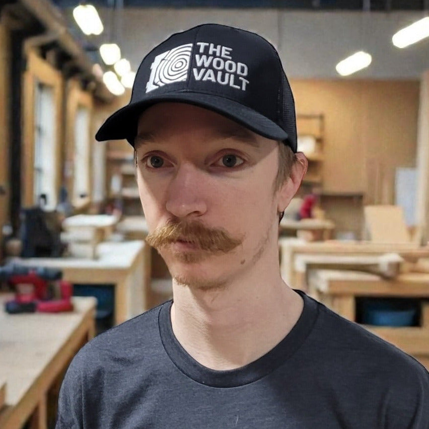 Man wearing a 'The Wood Vault' t-shirt and cap in a workshop.